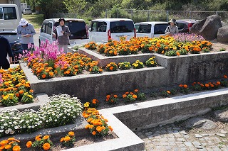 写真：数段になっている立体的な花壇にオレンジ色や黄色、ピンク色の花が咲いています